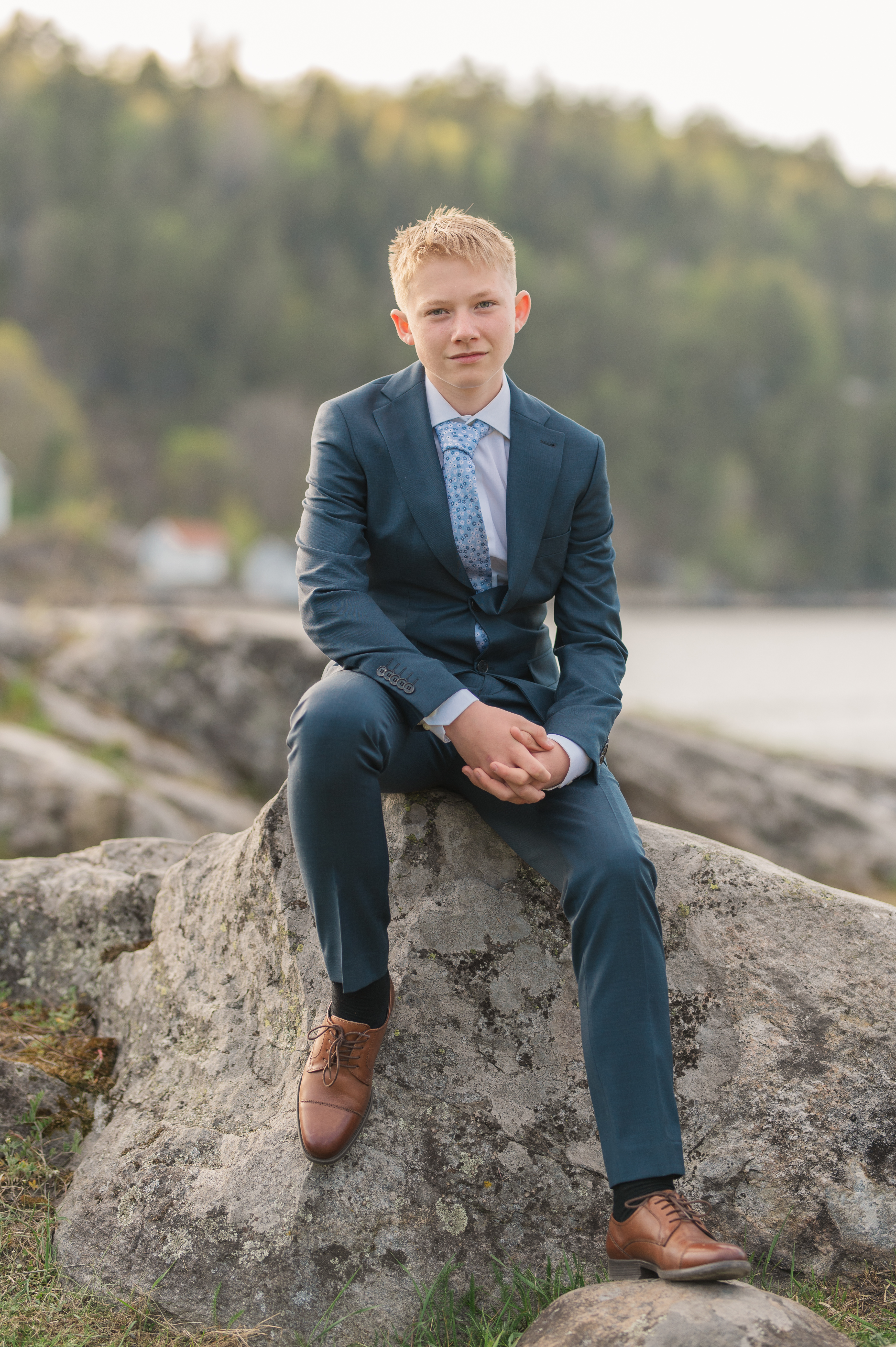 Konfirmantfotografering - Gutt i blå dress som sitter på en sten