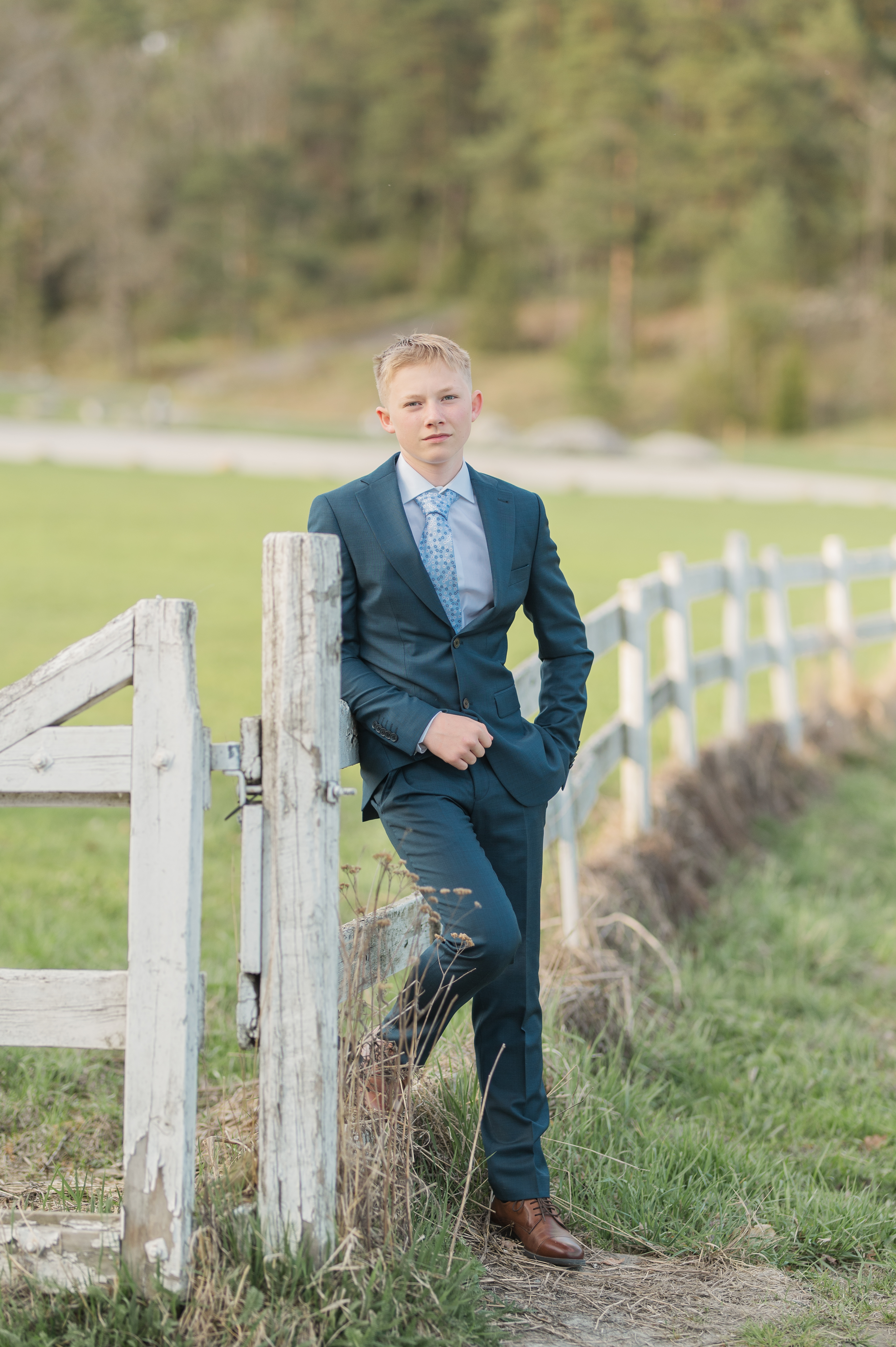 Konfirmantfotografering - Gutt i Blå dress som lener seg på gjerde